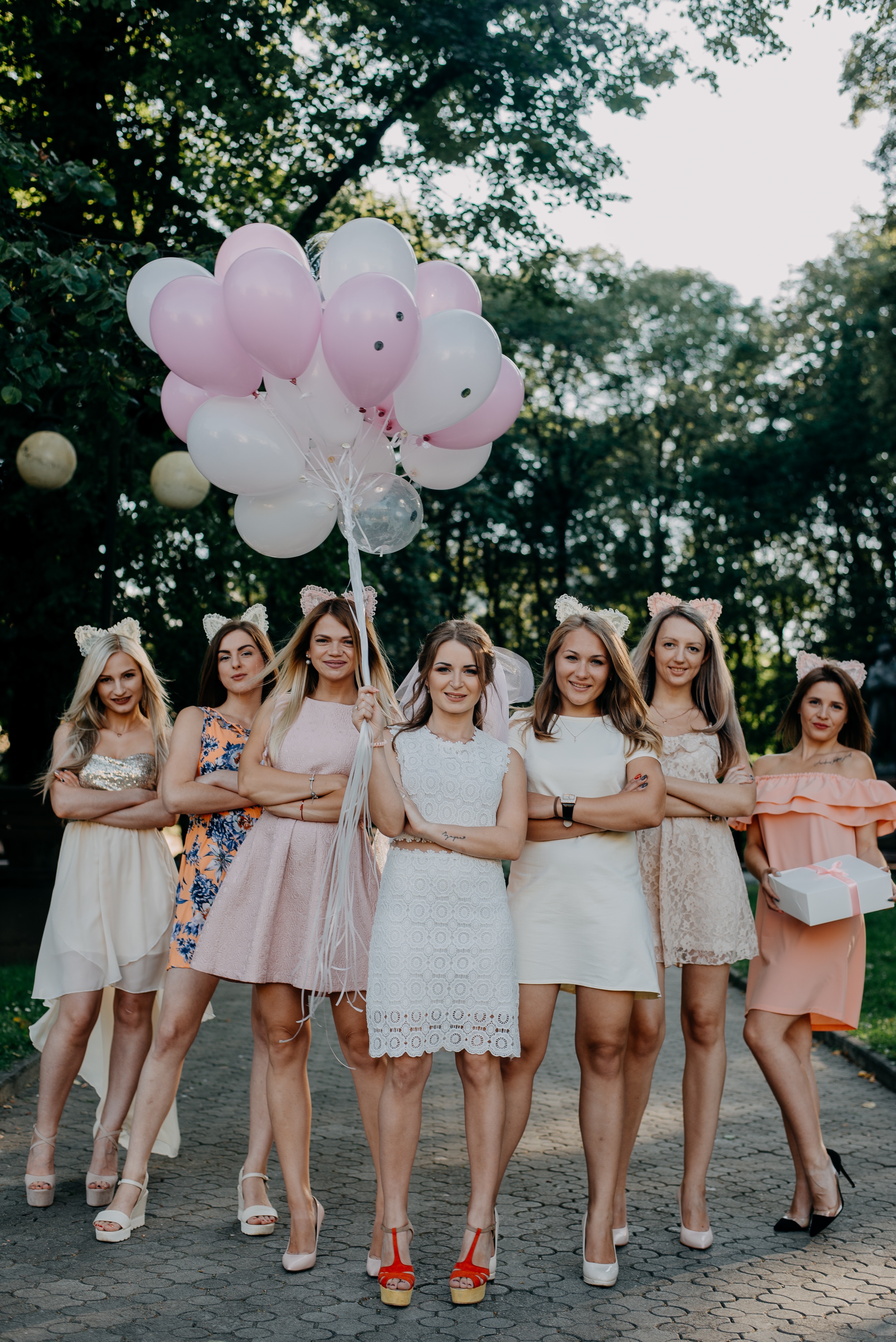 Bachelorette party planning image: A group of excited women wearing matching shirts and sashes, holding colorful cocktails and dancing, surrounded by decorations and balloons.